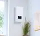 Weißer elektrischer Durchlauferhitzer der Marke Vaillant, wandmontiert, mit digitalem Display und Einstellungsregler, platziert in einem hellen Raum neben einer Pflanze.